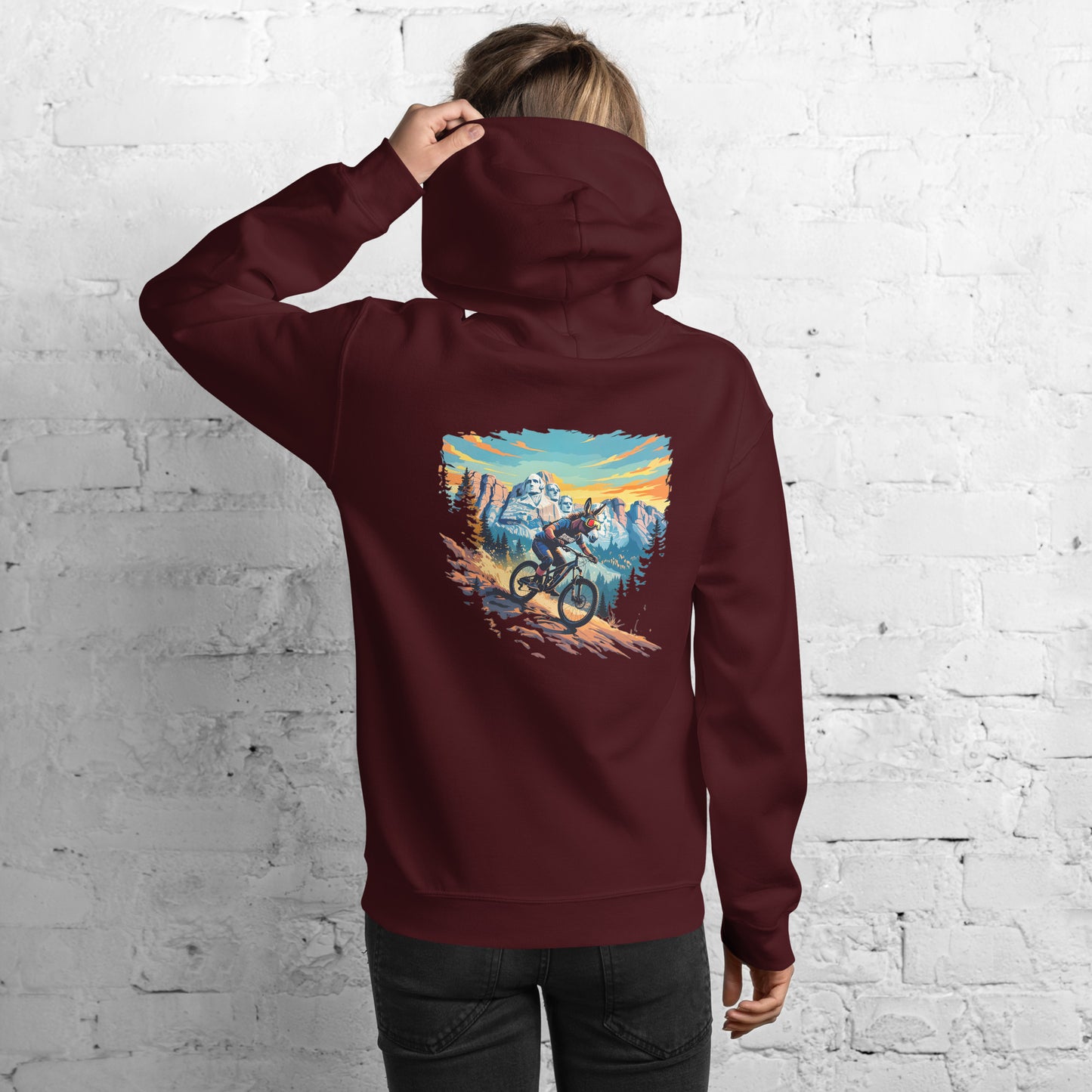 Person wearing a maroon hoodie with a mountain bike graphic on the back against a white brick wall.