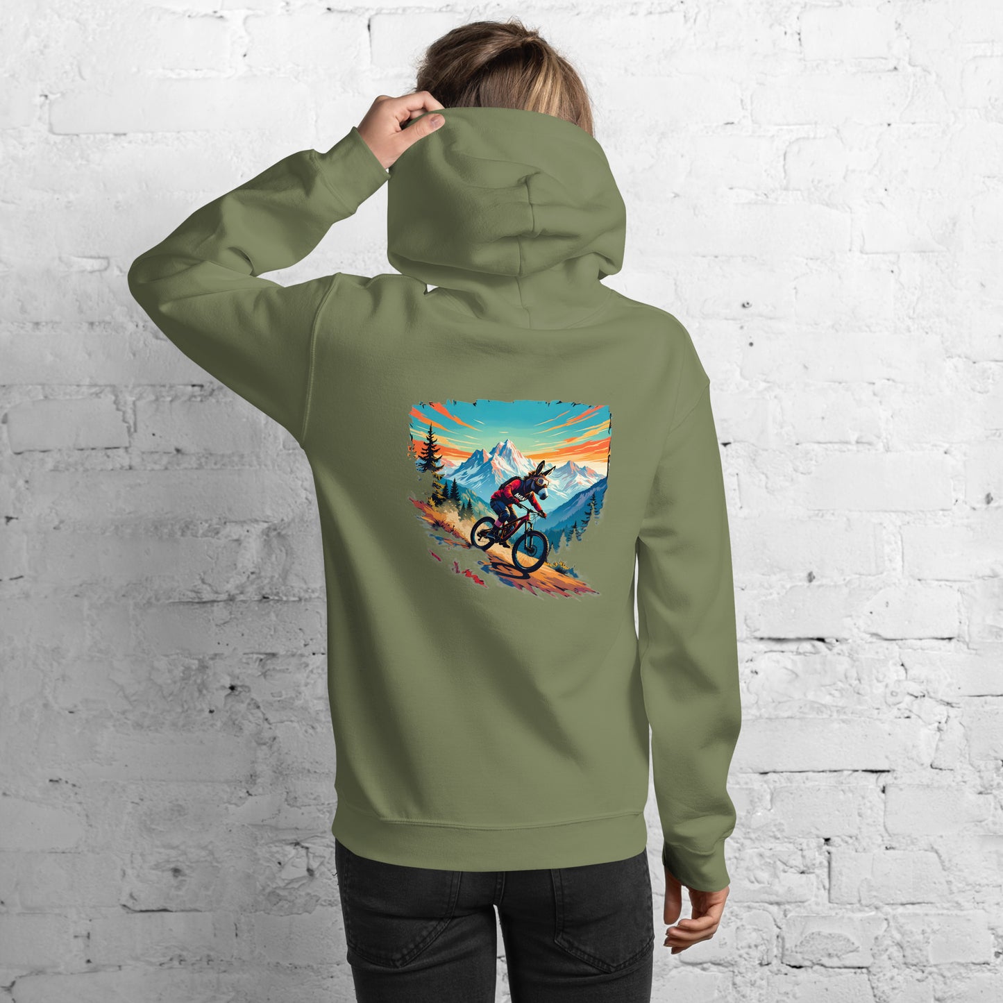 Person wearing a green hoodie with a mountain bike design on the back against a white brick wall.