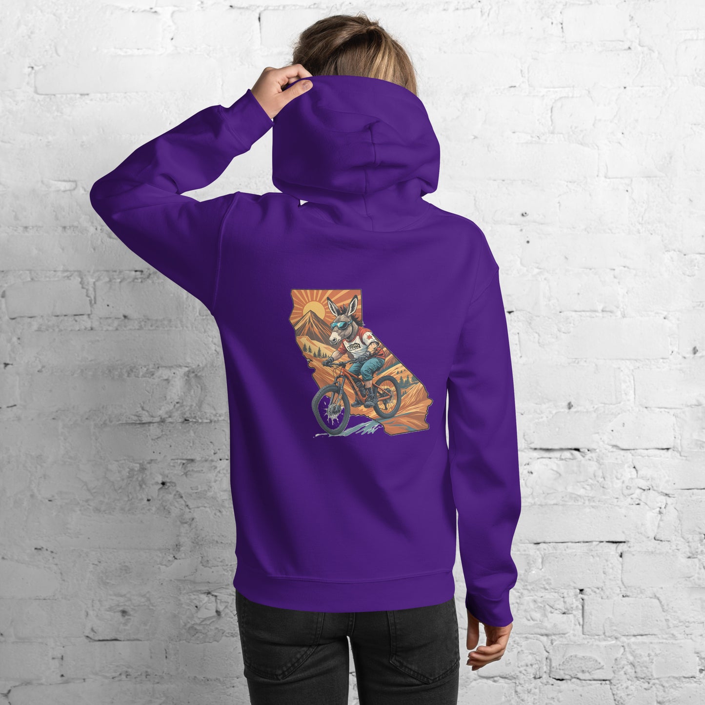 Person wearing a purple hoodie with a colorful graphic on the back, standing against a white brick wall.