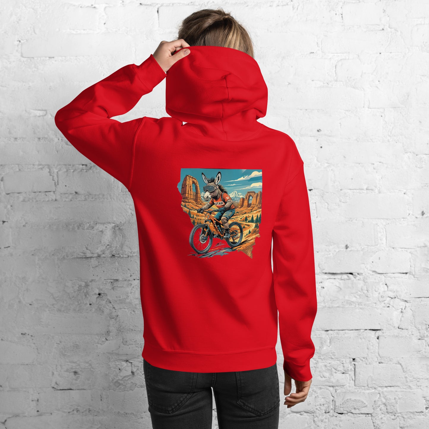 Person wearing a red hoodie with a graphic design on the back against a white brick wall.