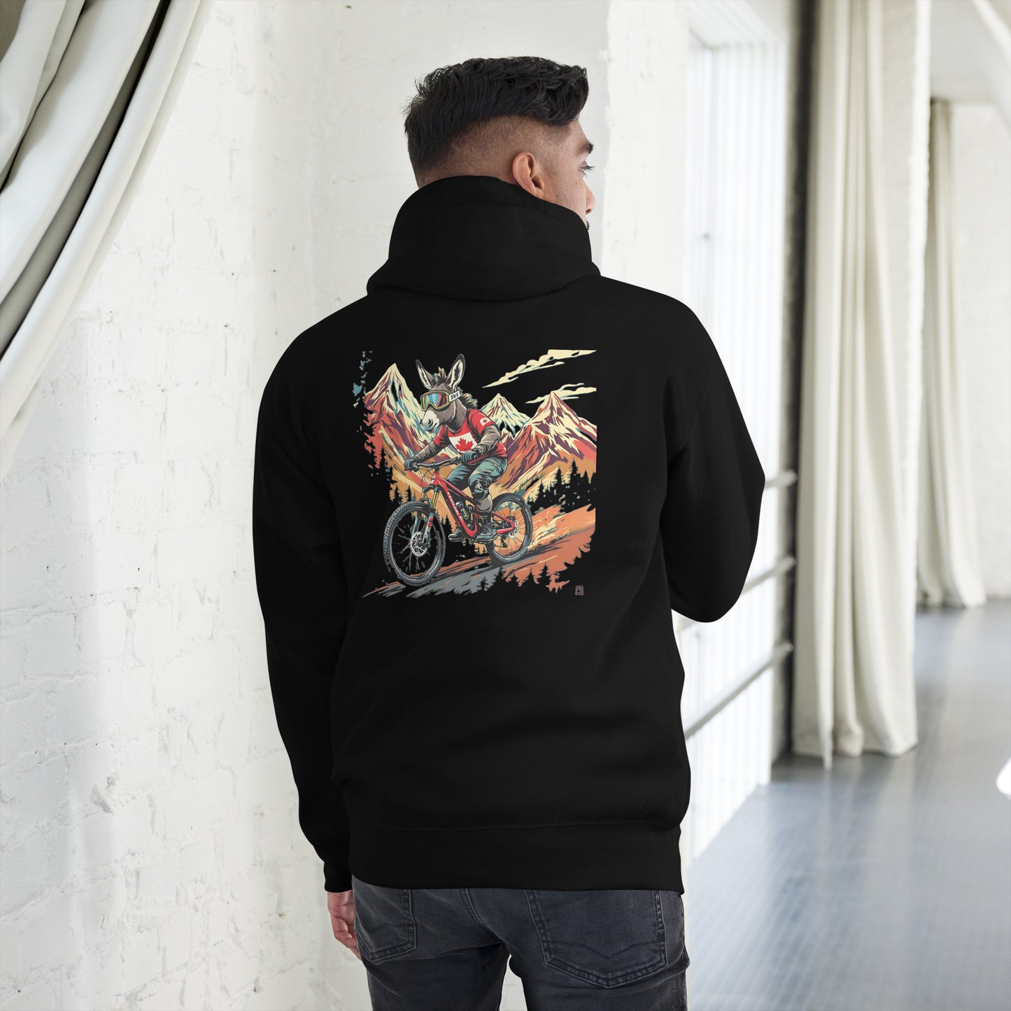 Person wearing a black hoodie with a colorful graphic on the back, standing in a room with white walls and gray floor.
