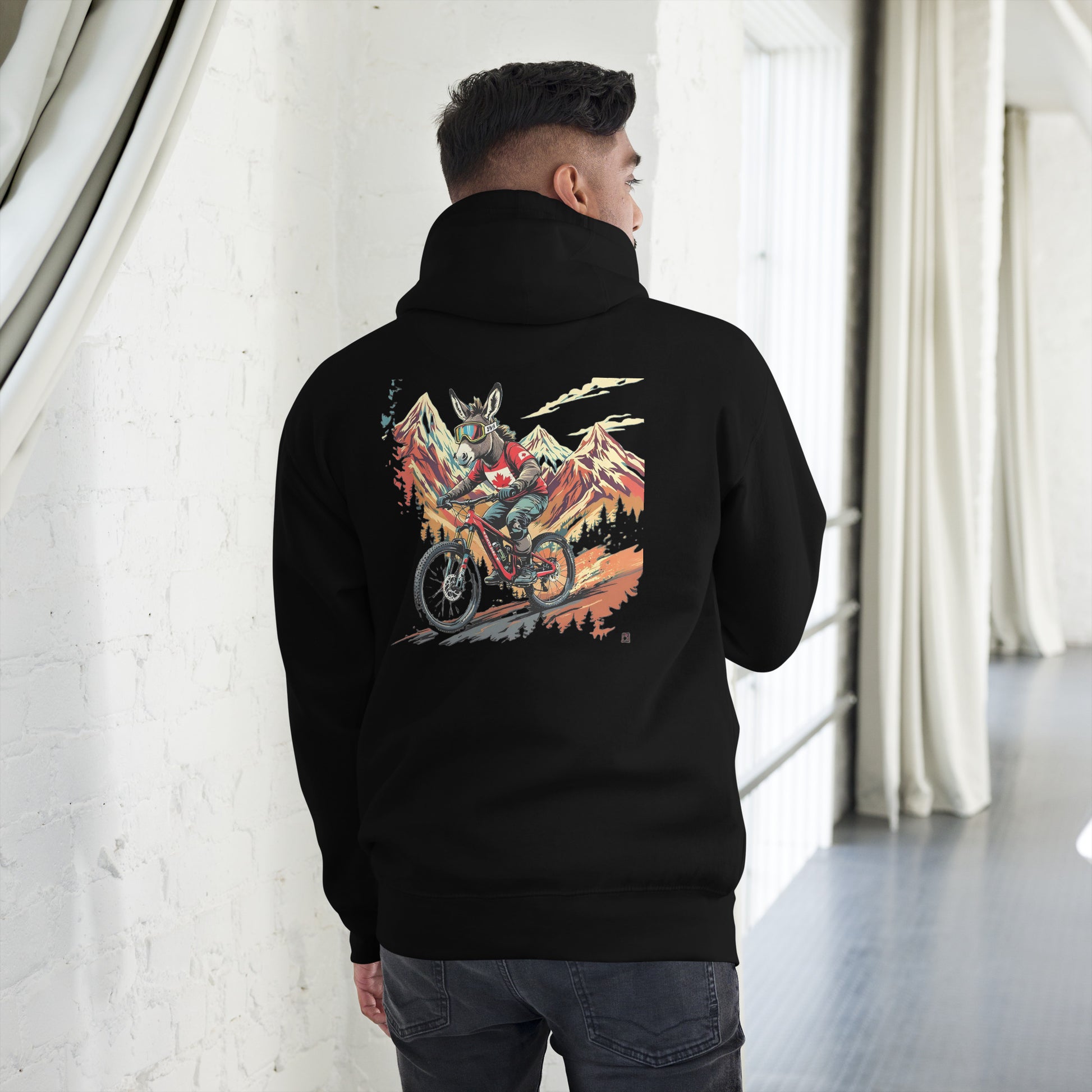 Person wearing a black hoodie with a colorful graphic on the back, standing in a room with white walls and gray floor.