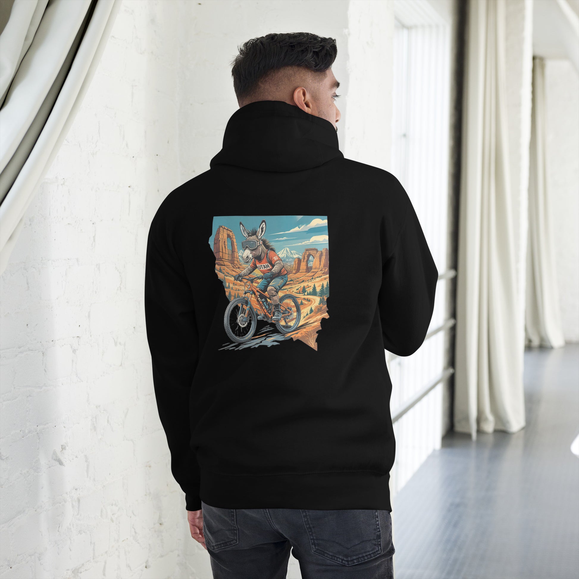 Person wearing a black hoodie with a colorful graphic on the back, standing in a room with white walls and gray floor.
