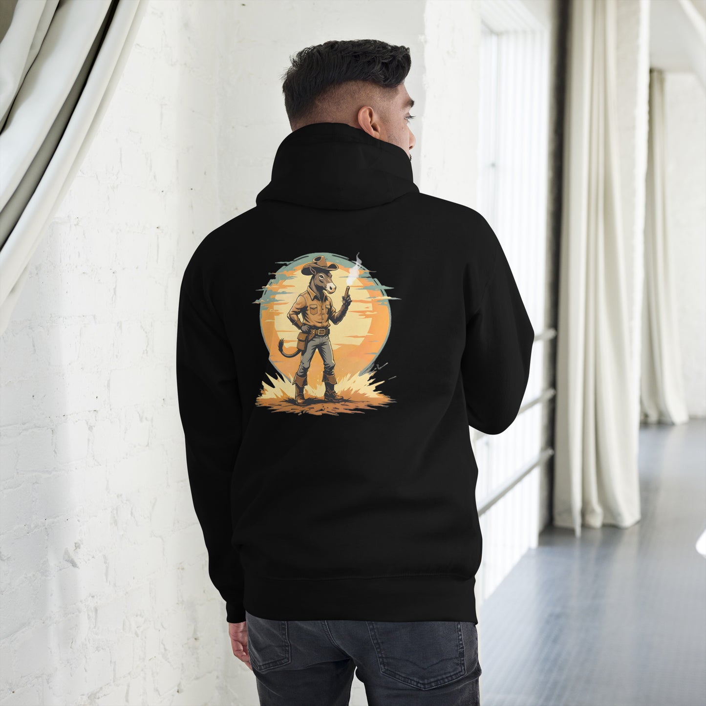 Person wearing a black hoodie with a graphic design on the back, standing in a room with white walls and a gray floor.