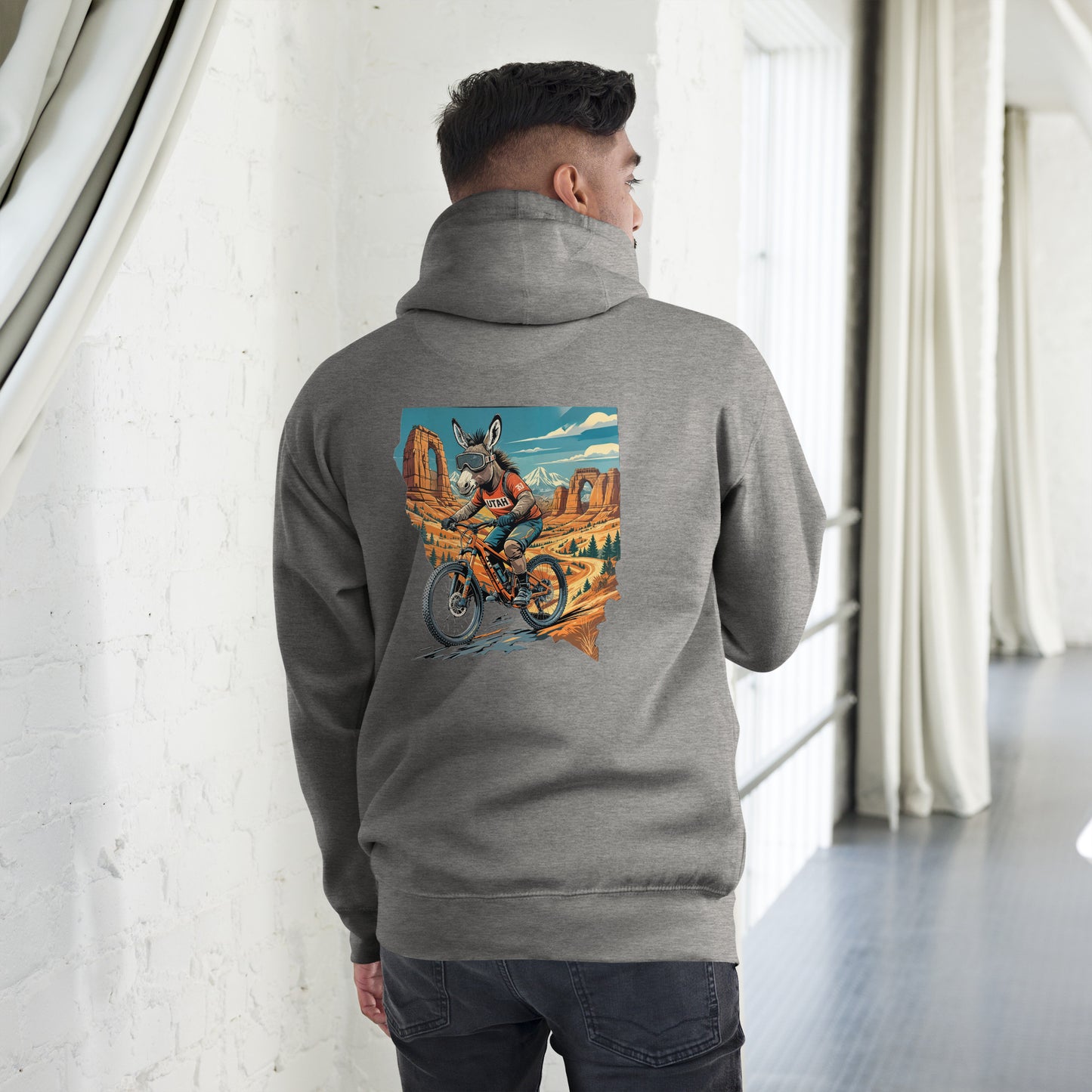 Person wearing a gray hoodie with a colorful graphic on the back, standing in a room with white walls and a window.