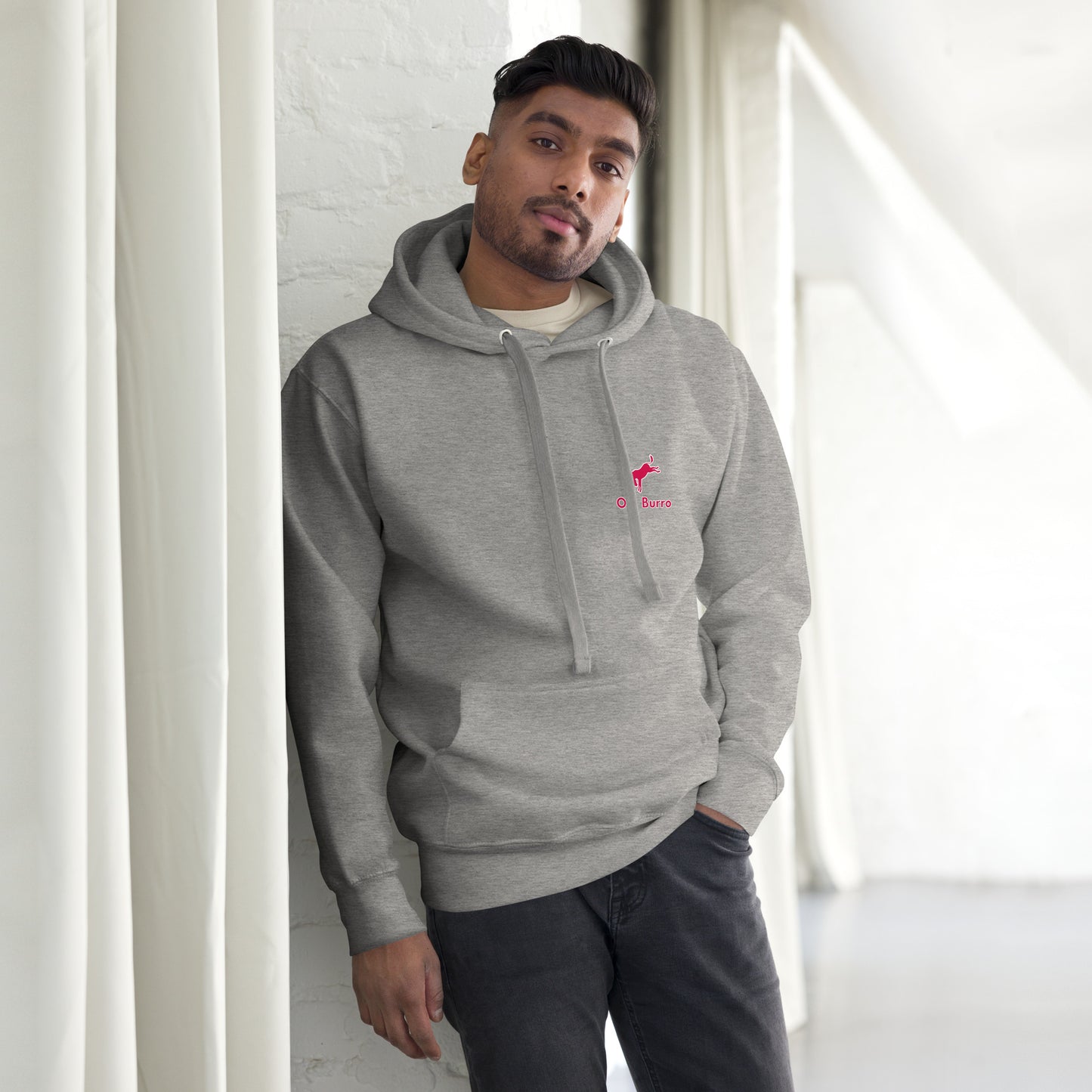 Man wearing a gray hoodie with a logo, standing against a white wall.