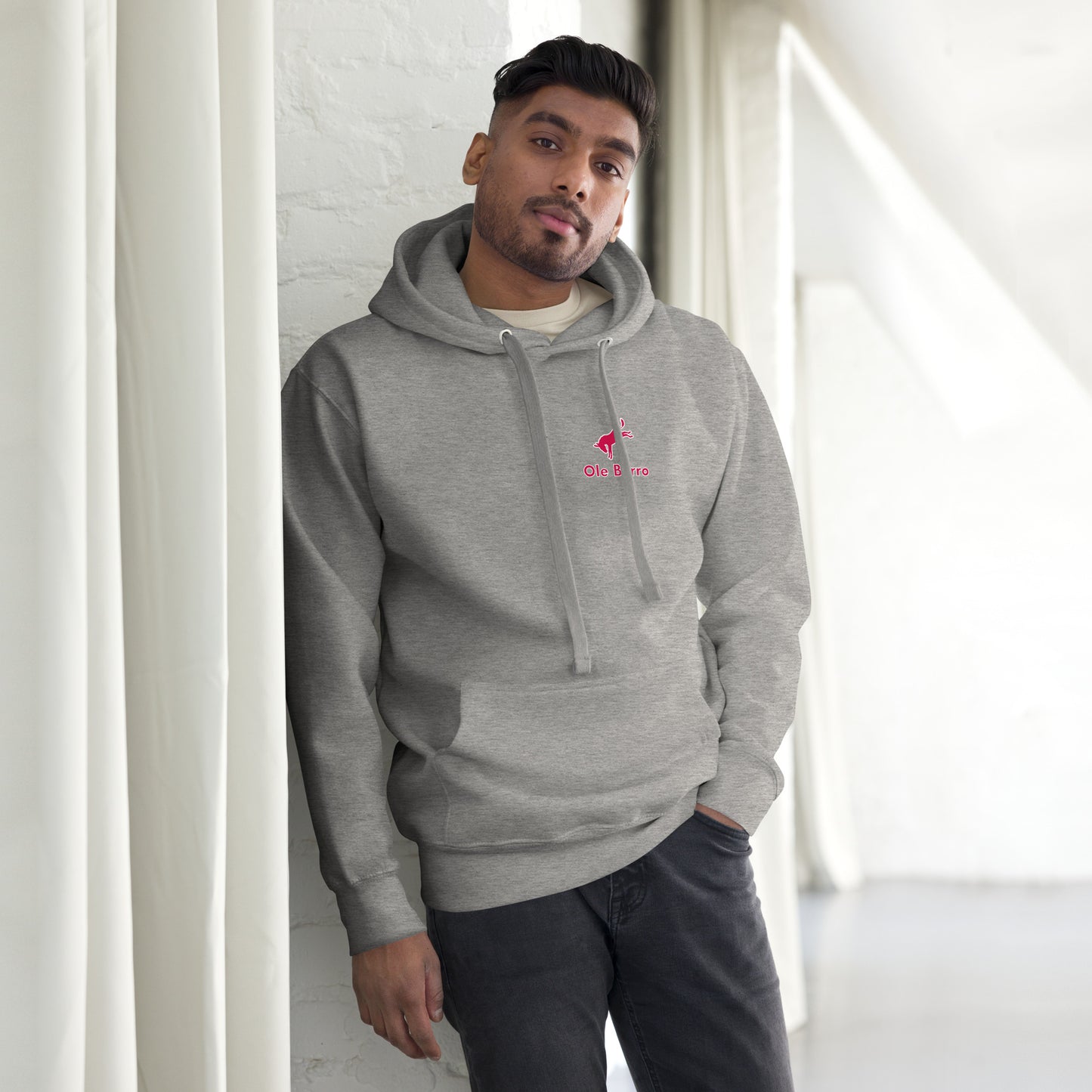 Man wearing a gray hoodie with a logo, standing against a white wall.