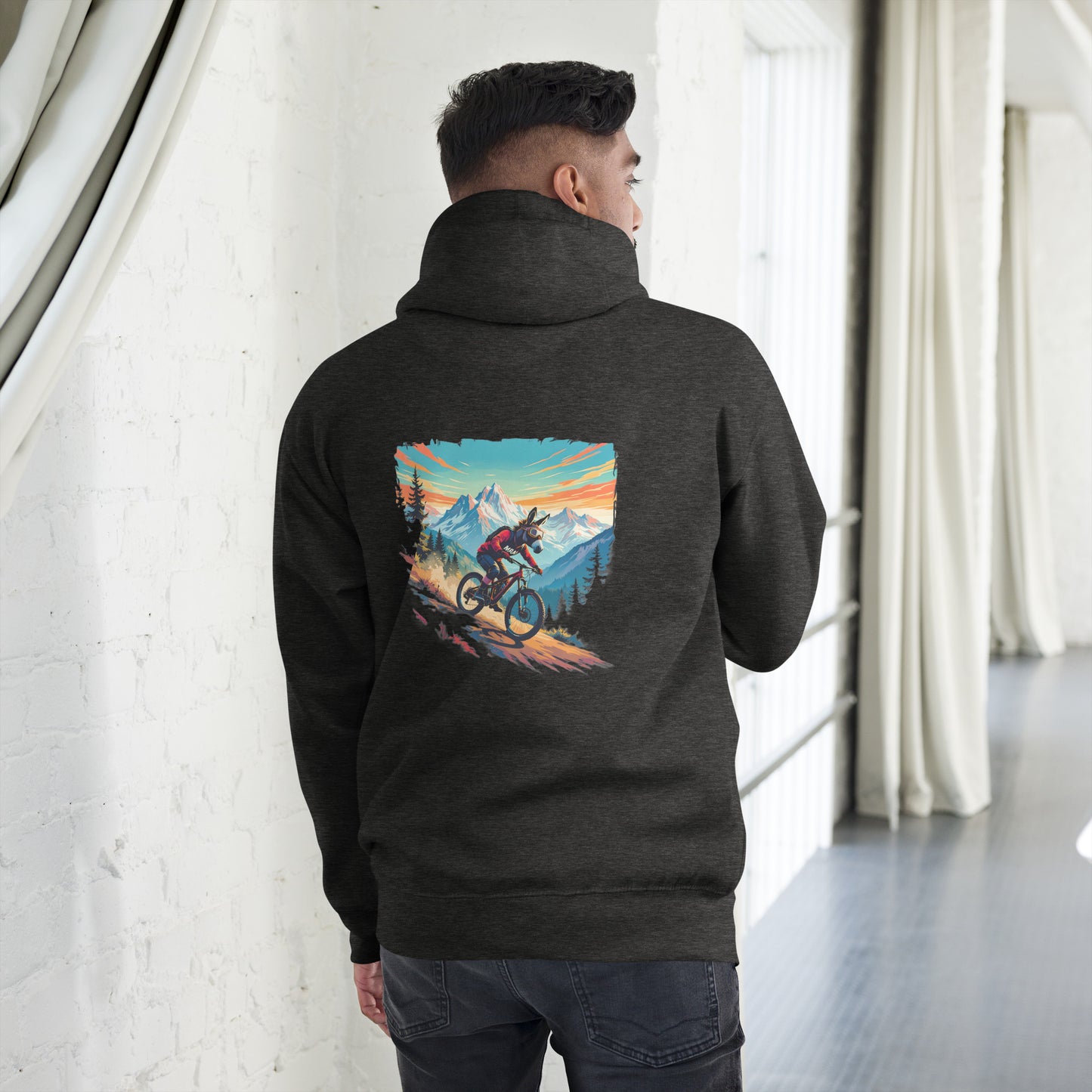Person wearing a black hoodie with a mountain bike graphic on the back, standing in a room with white walls and curtains.