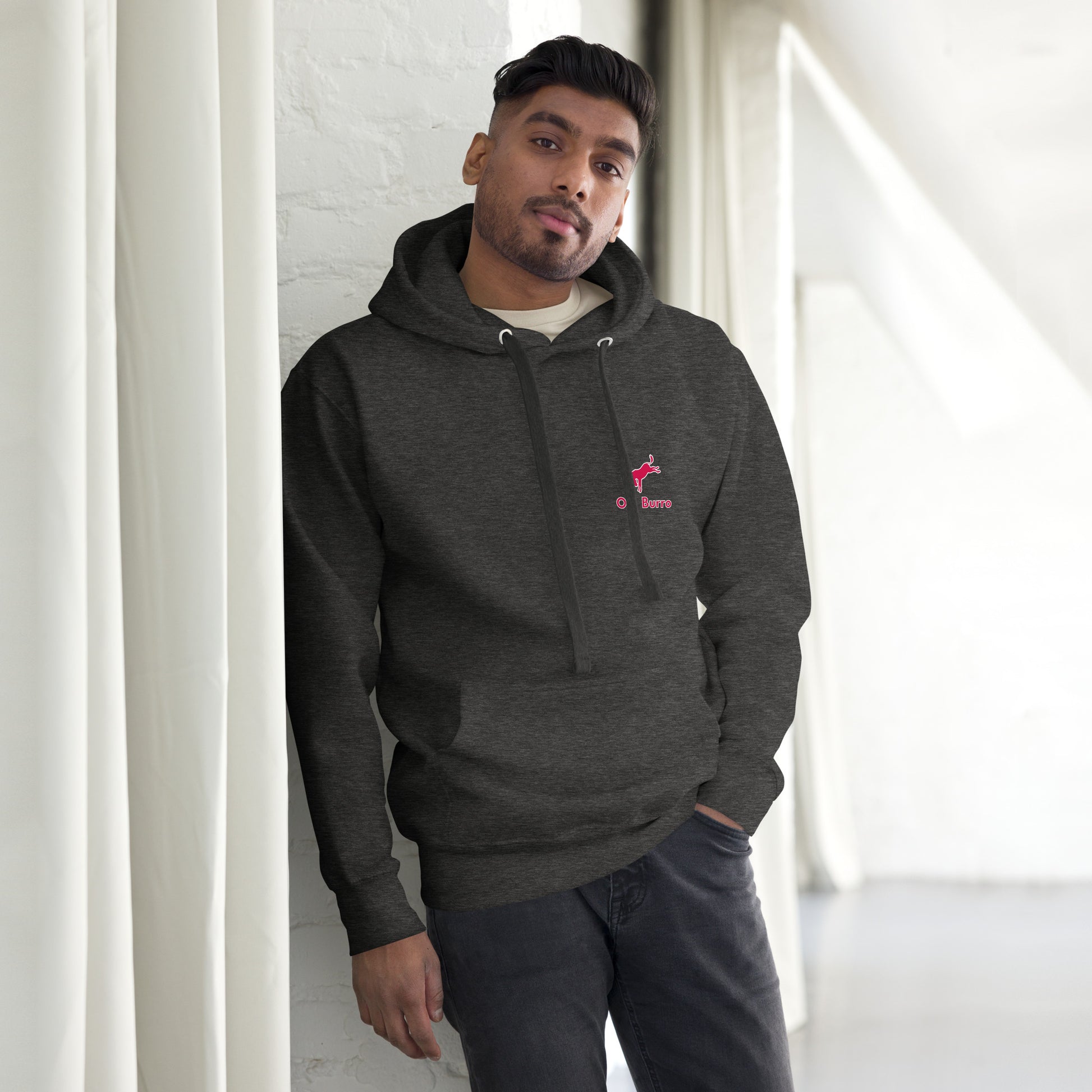 Man wearing a dark gray hoodie with a logo, standing against a white wall.