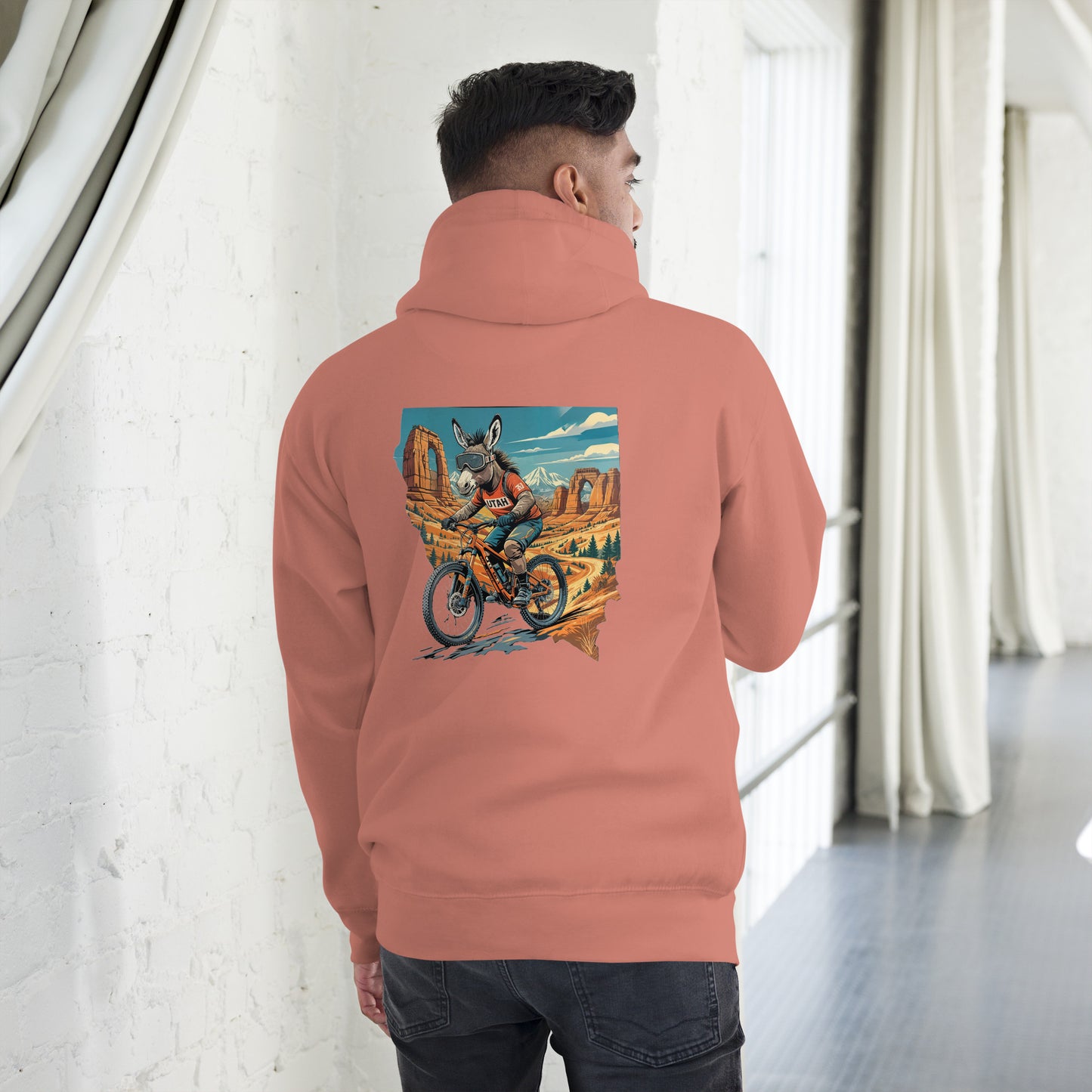 Person wearing a peach hoodie with a colorful graphic on the back, standing in a room with white walls and a gray floor.