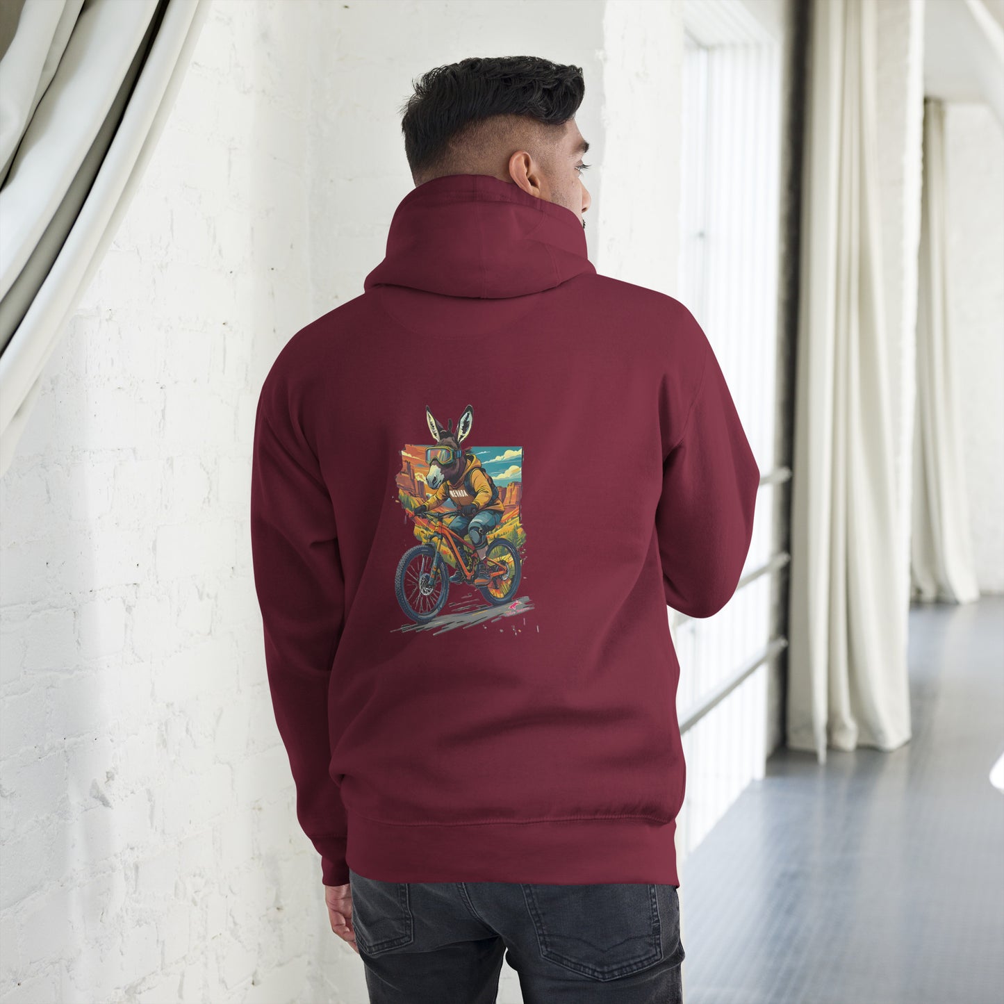 Person wearing a maroon hoodie with a colorful graphic on the back, standing in a room with white walls and curtains.