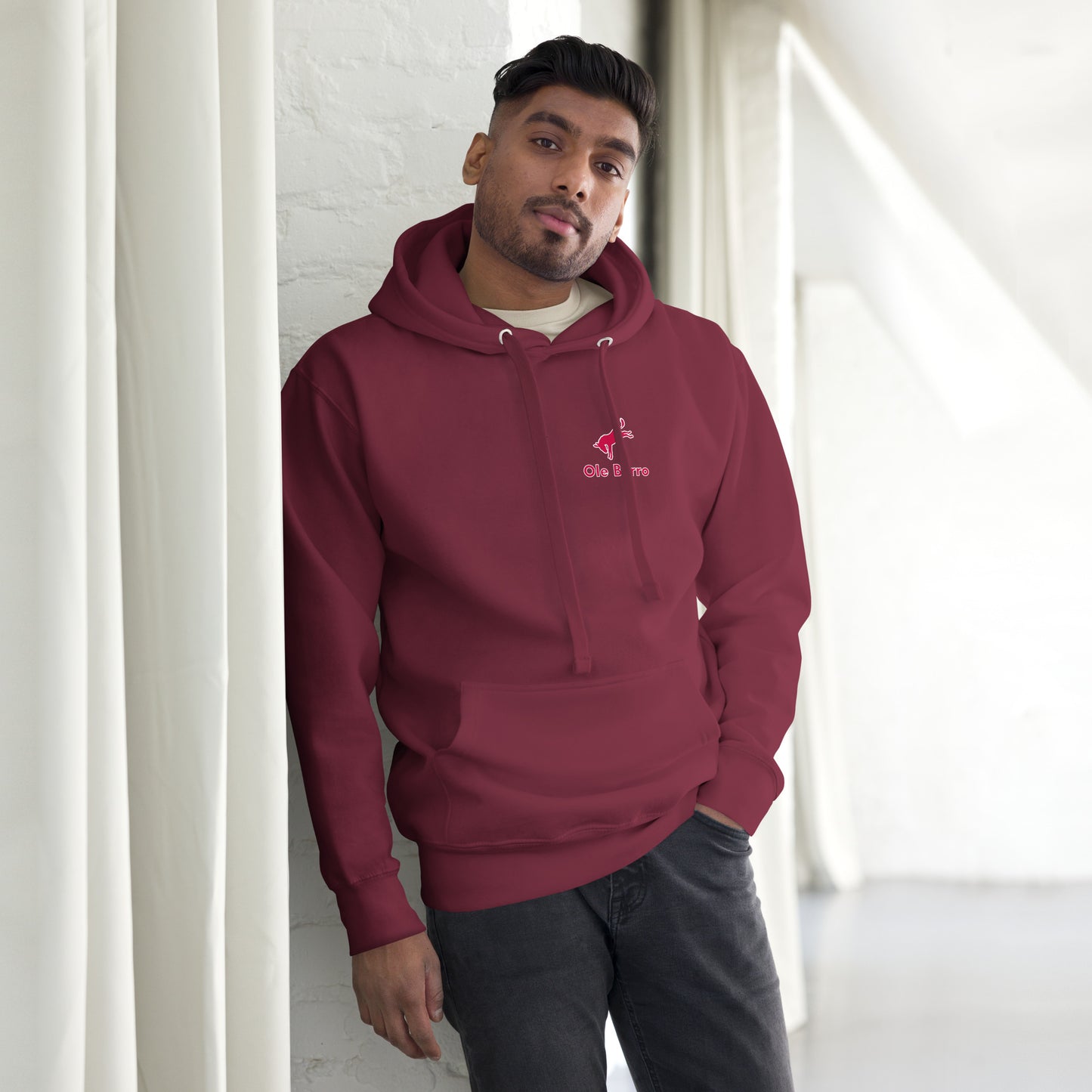 Man wearing a maroon hoodie with a logo, standing against a white wall.