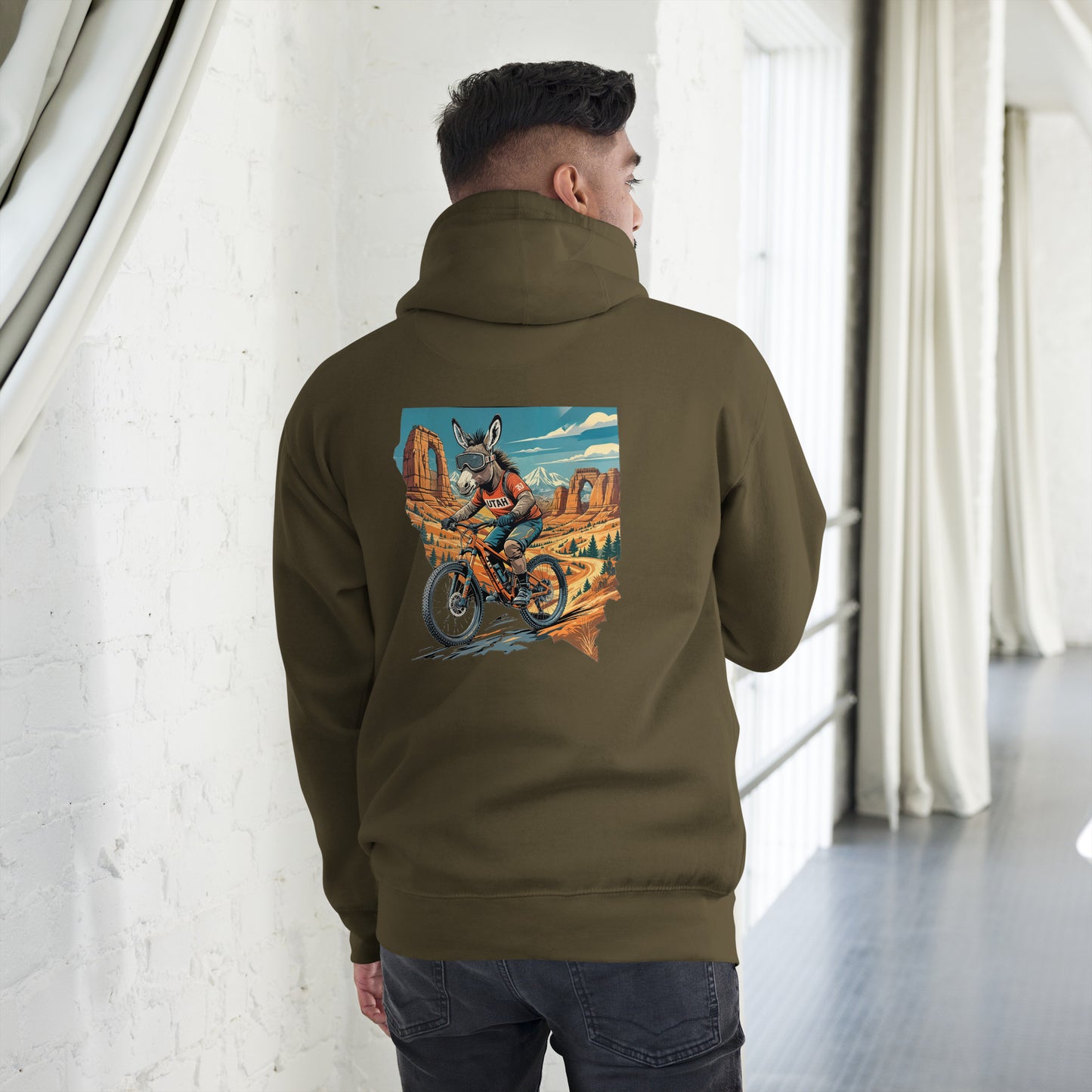 Person wearing a green hoodie with a colorful graphic on the back, standing in a room with white walls and a gray floor.