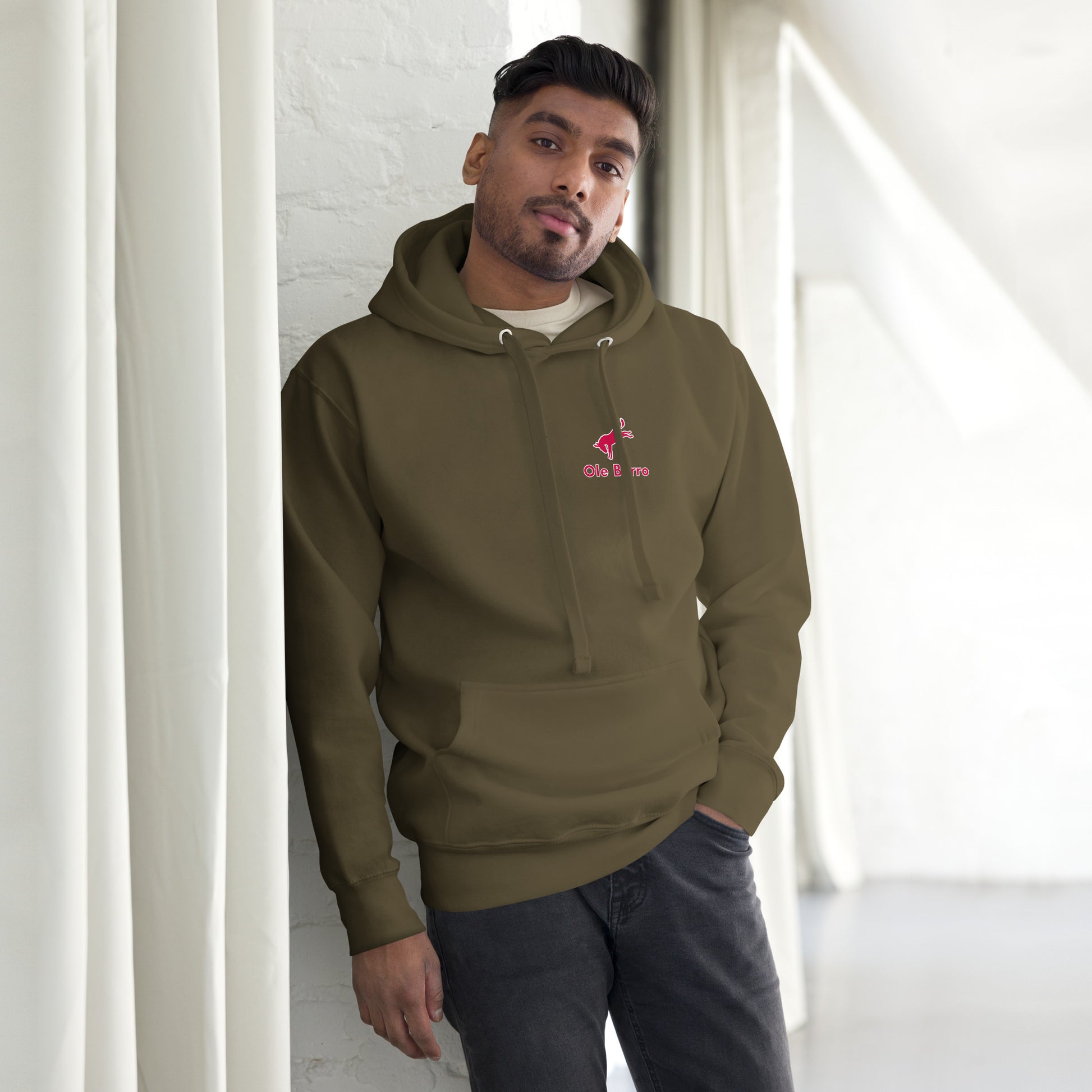 Man wearing a green hoodie with a logo, standing against a white wall.