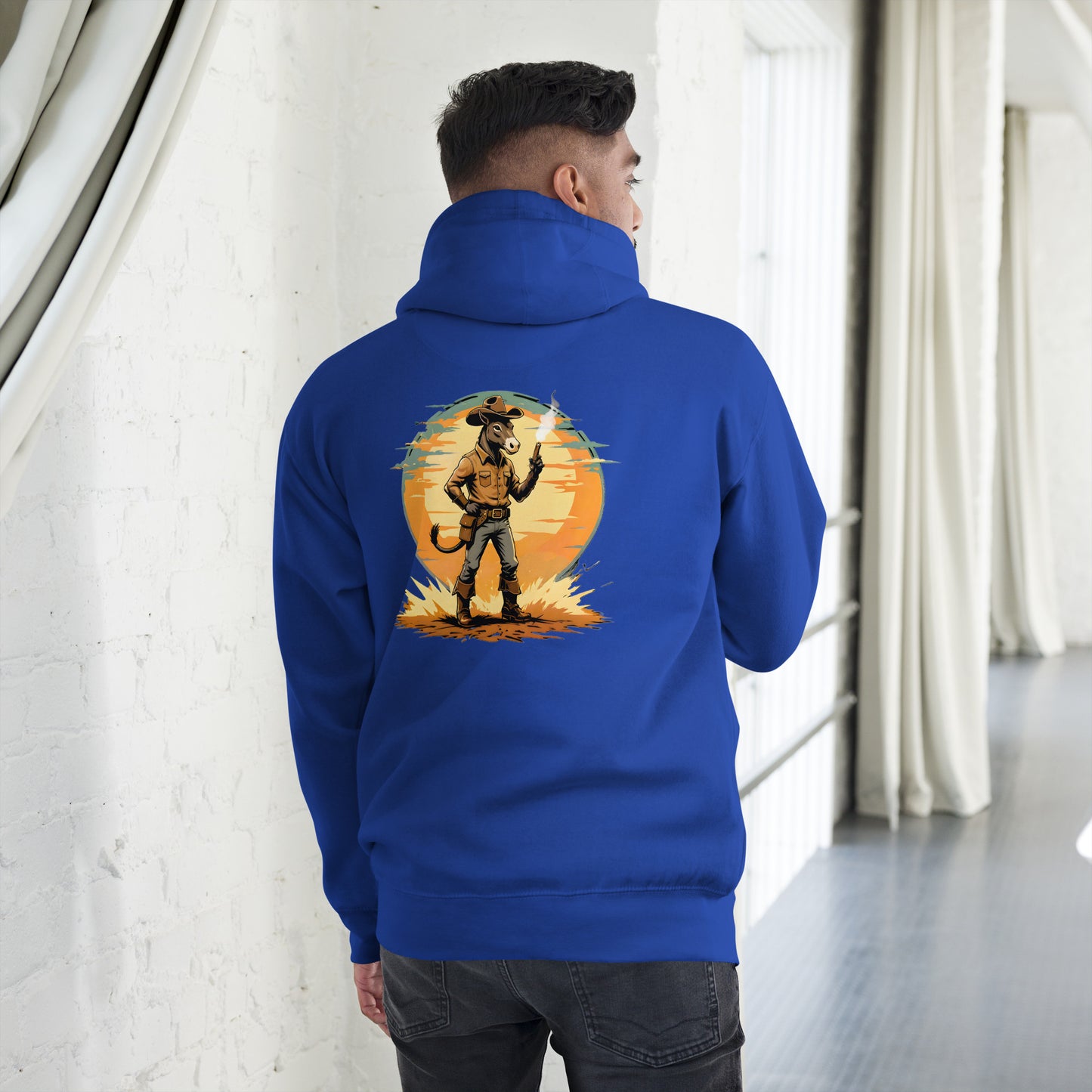 Person wearing a blue hoodie with a graphic design on the back, standing in a room with white walls and gray floor.