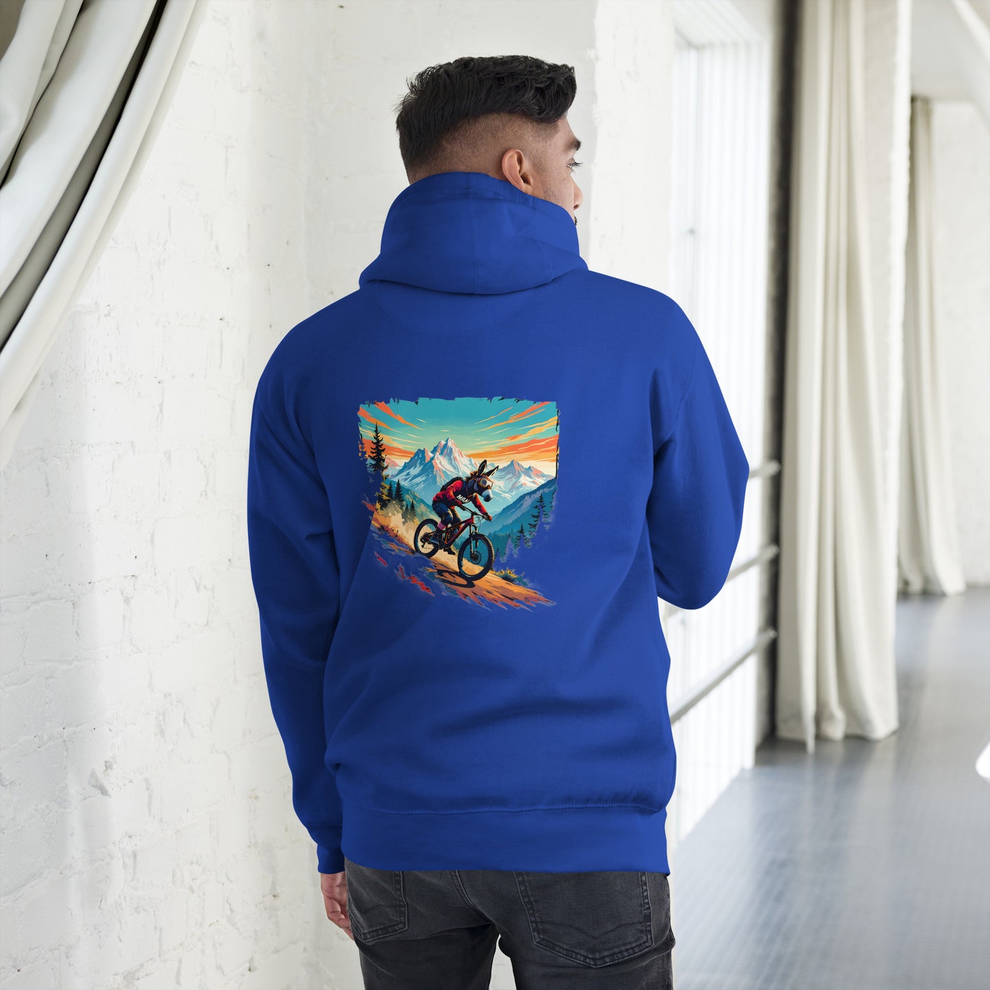 Person wearing a blue hoodie with a mountain bike graphic on the back, standing in a room with white walls and curtains.