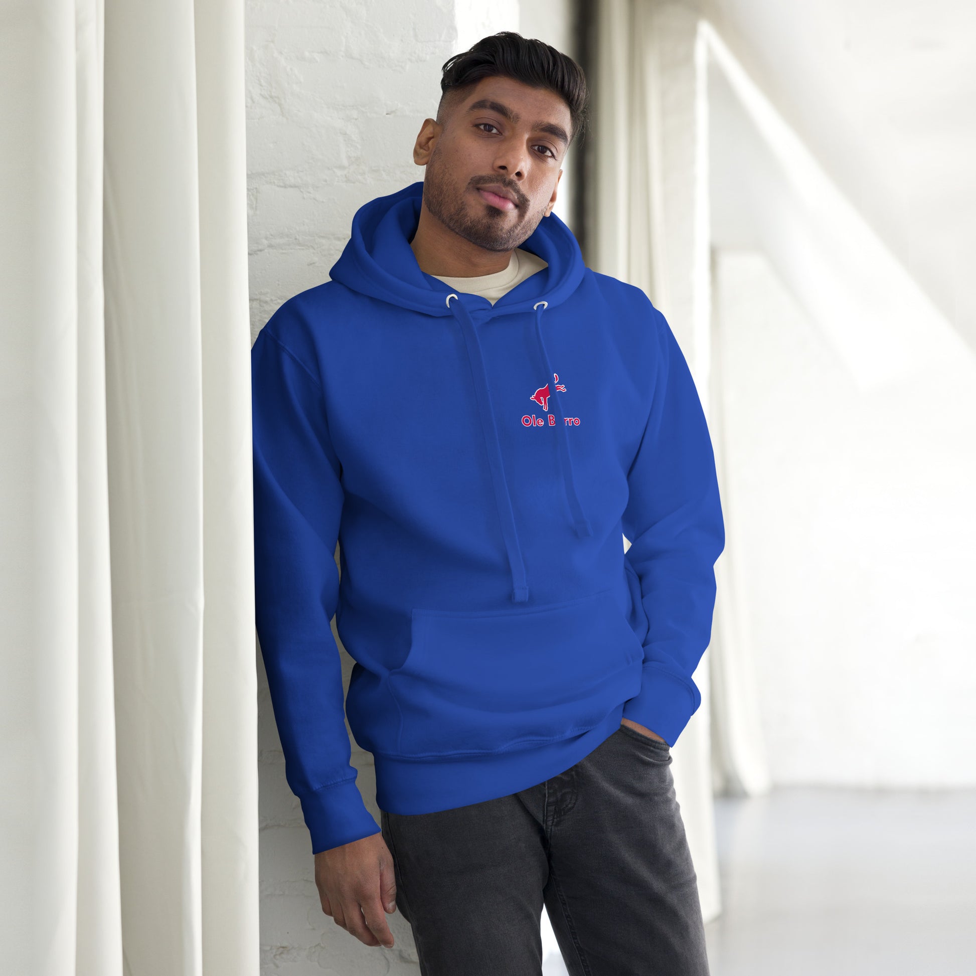 Man wearing a blue hoodie with a logo, standing against a white wall.