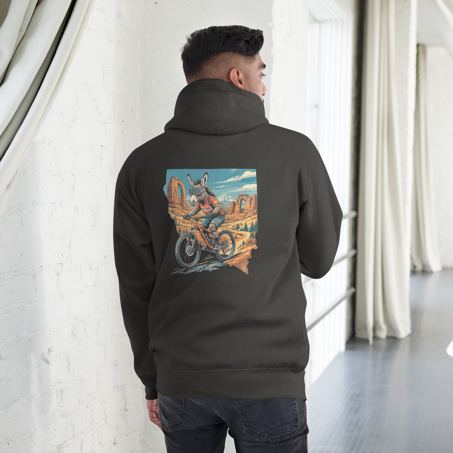 Person wearing a black hoodie with a colorful graphic on the back, standing in a room with white walls and curtains.