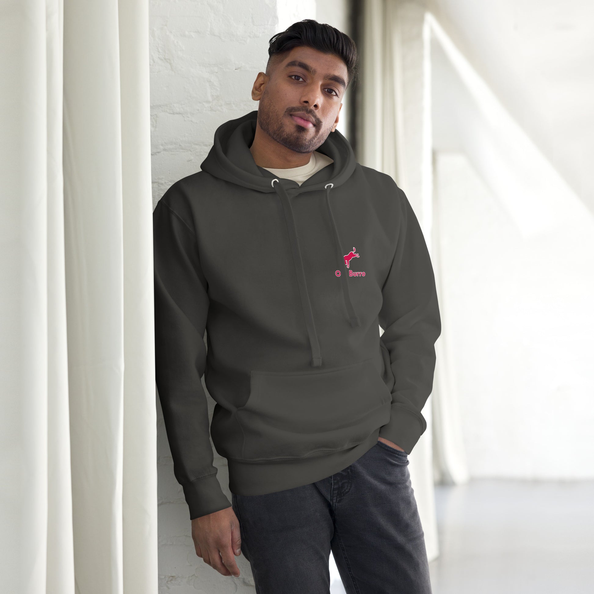 Man wearing a dark gray hoodie with a logo, standing against a white wall.