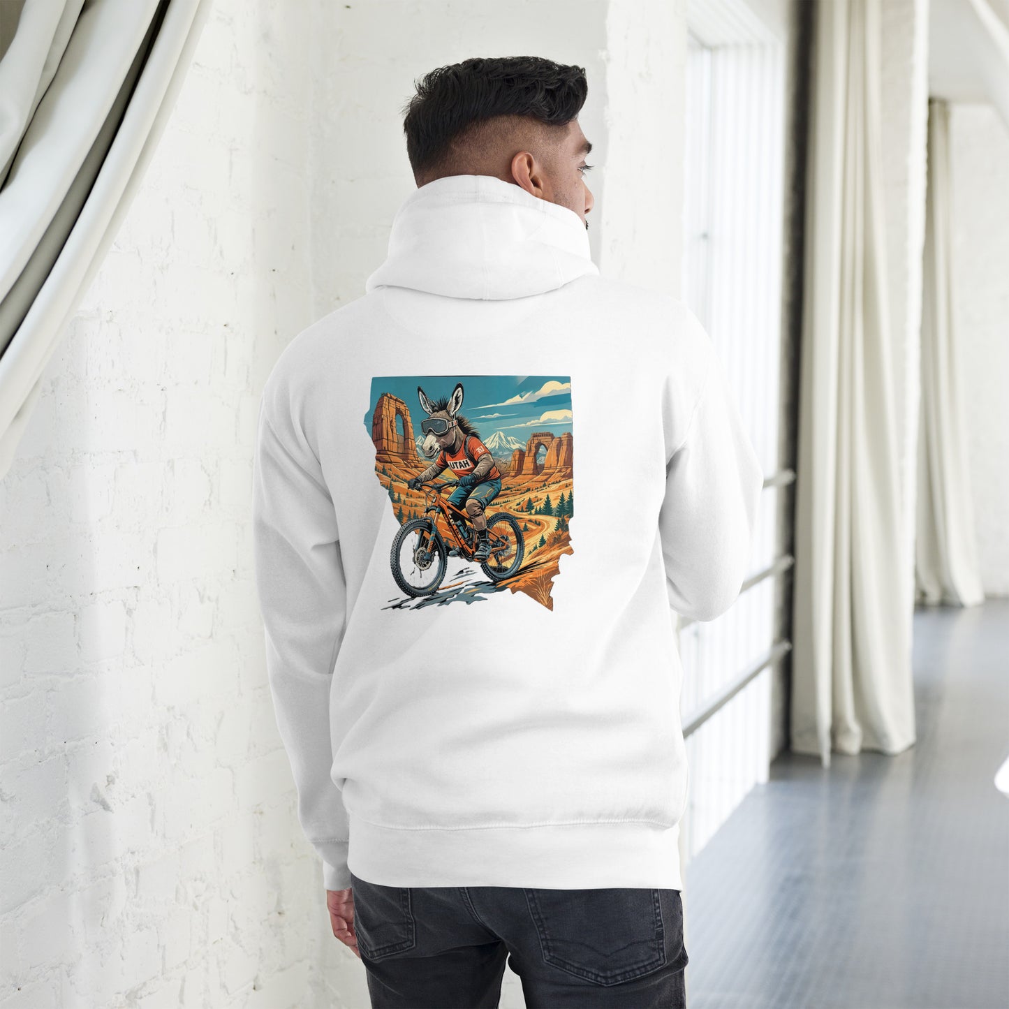 Person wearing a white hoodie with a colorful graphic on the back, standing in a room with white walls and curtains.