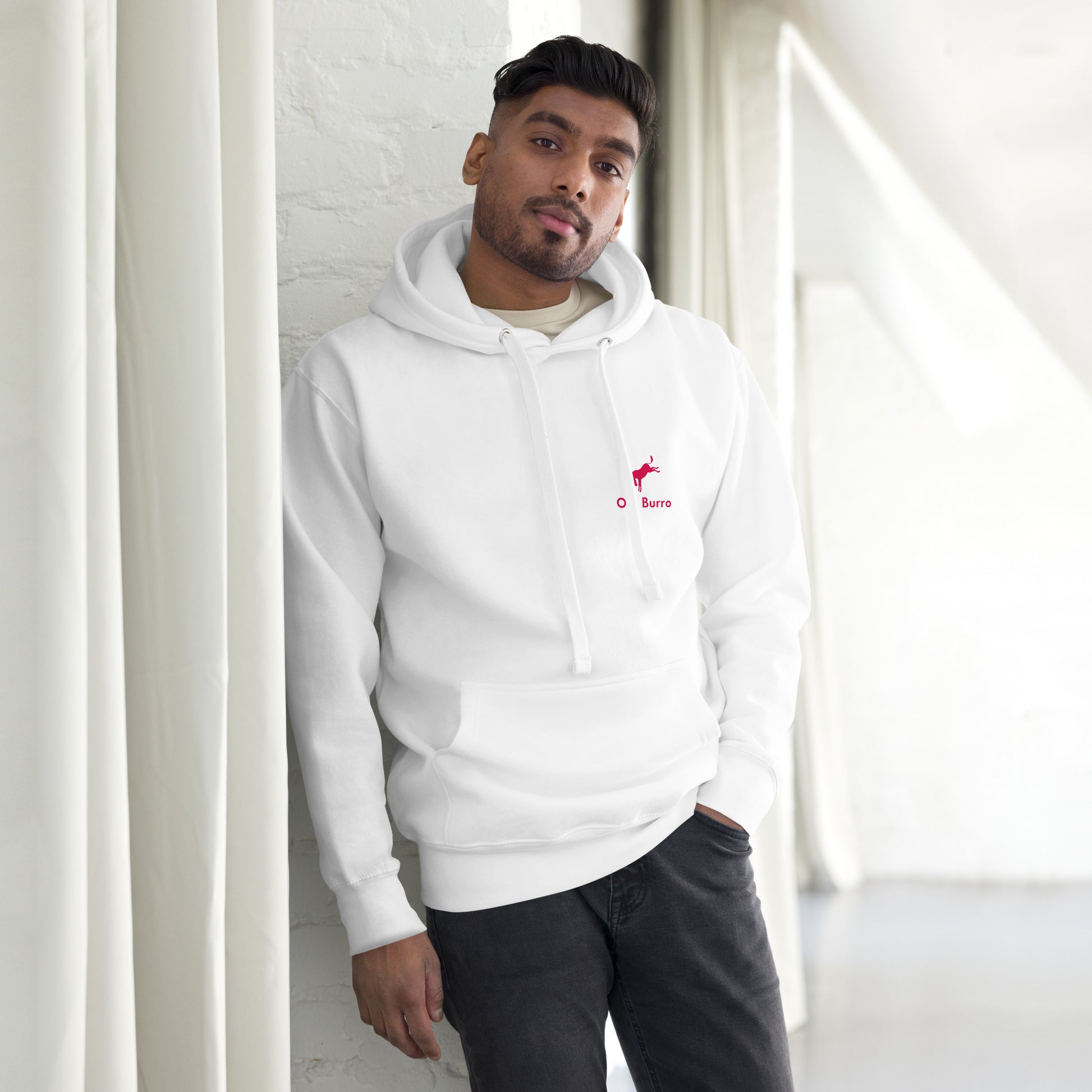Man wearing a white hoodie with a logo, standing indoors against a light-colored wall.