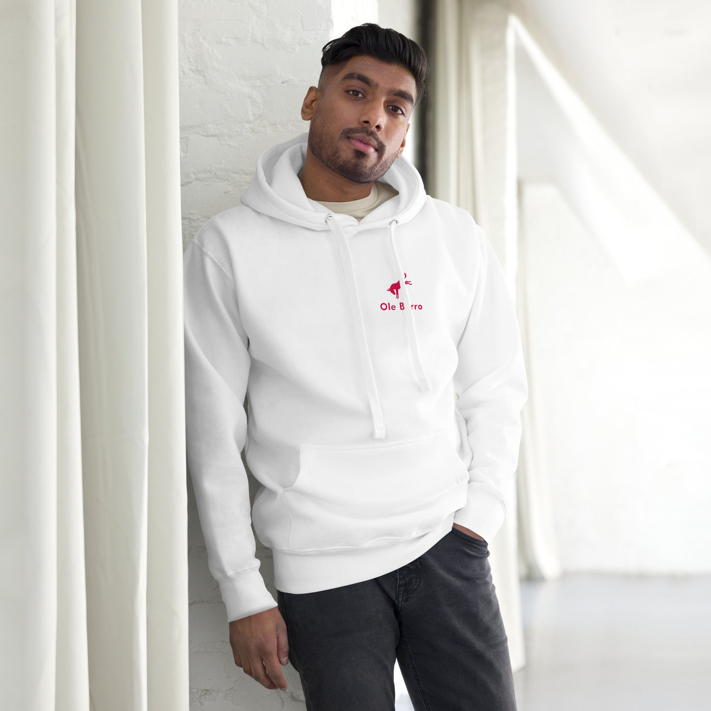 Man wearing a white hoodie with a logo, standing indoors against a light-colored wall.