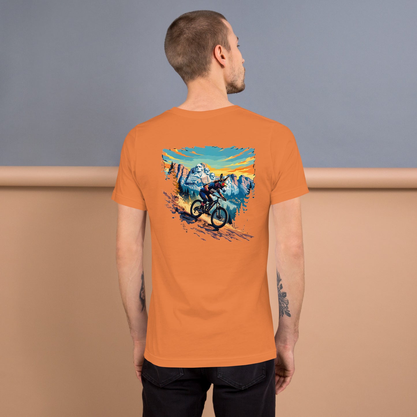 Man wearing an orange t-shirt with a mountain bike graphic on the back, standing against a plain background.
