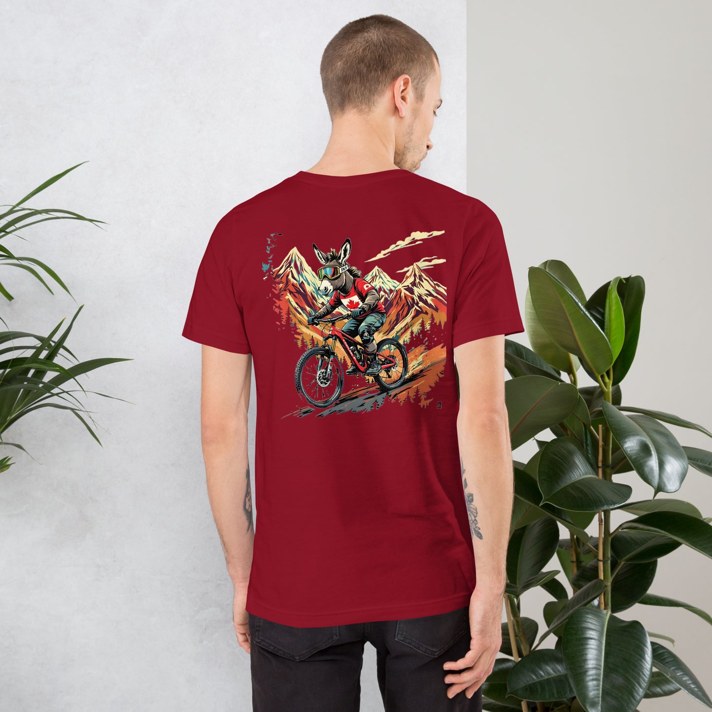 Person wearing a red t-shirt with a graphic design on the back, standing against a light gray wall with plants.