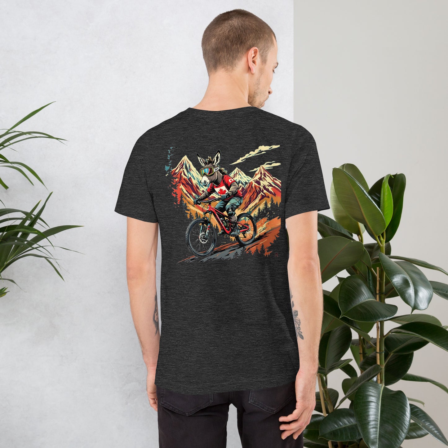 Person wearing a black t-shirt with a colorful graphic on the back, standing against a light gray wall with plants.