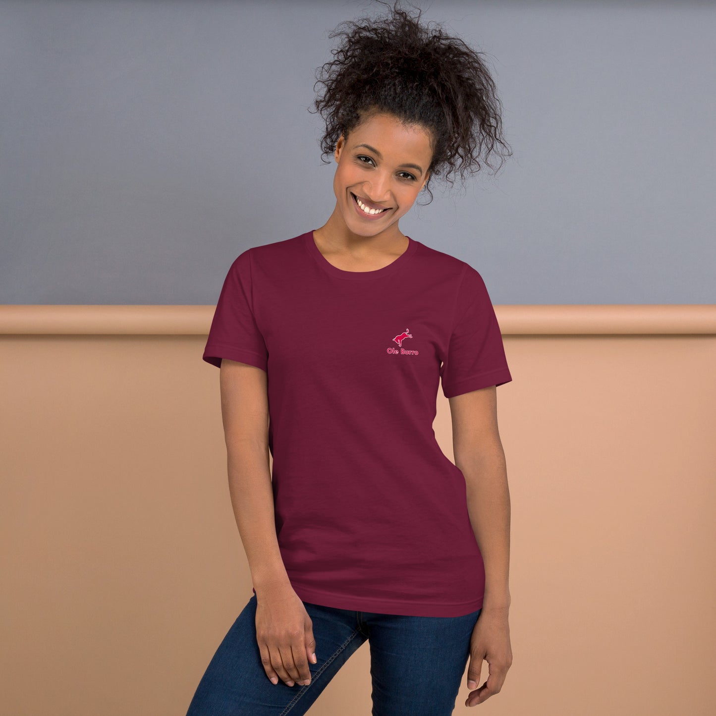 Woman wearing a maroon t-shirt with a logo against a plain background