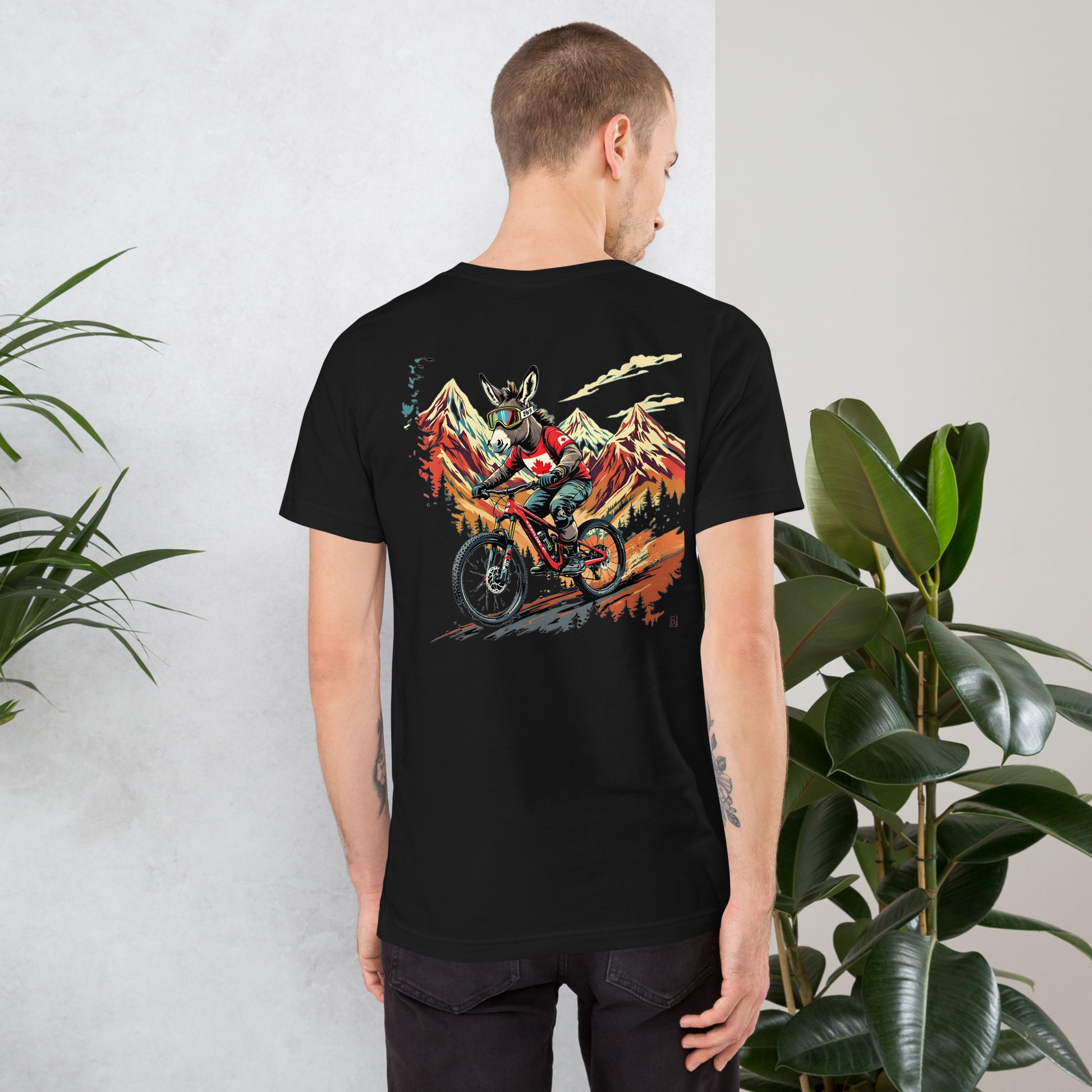 Person wearing a black t-shirt with a colorful graphic on the back, standing against a light gray wall with plants.