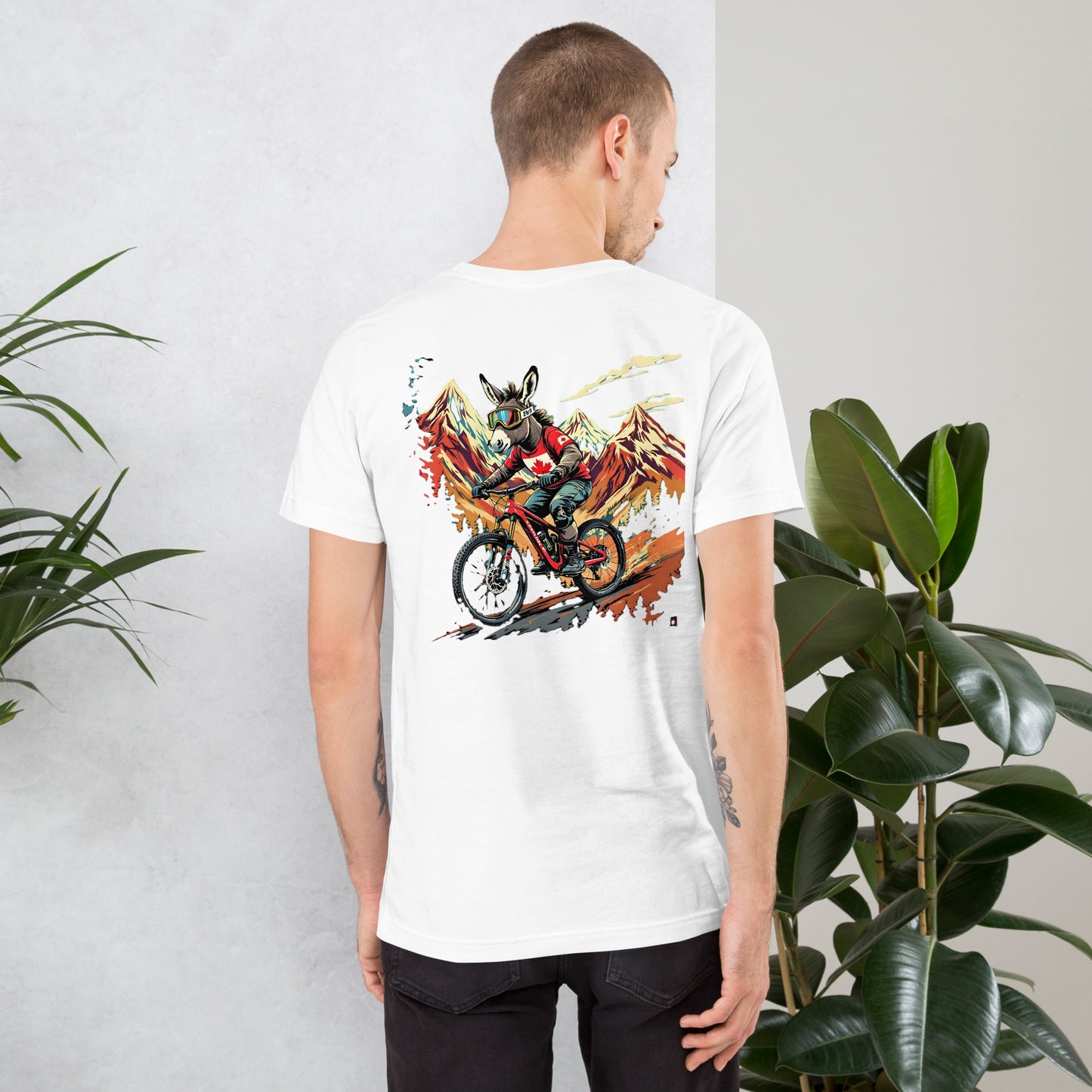 Person wearing a white t-shirt with a colorful graphic design on the back, standing against a light gray wall with plants.